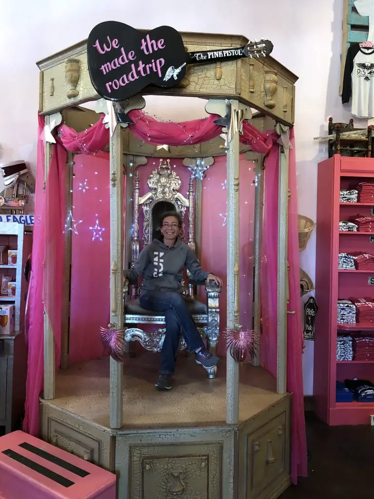 Grace sitting on a throne at The Pink Pistol Lindale Texas with a sign which says we made the roadtrip