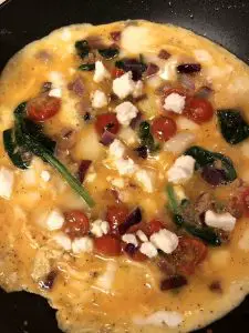 Egg with feta, spinach, tomatoes, garlic and red onion starting to set in a pan
