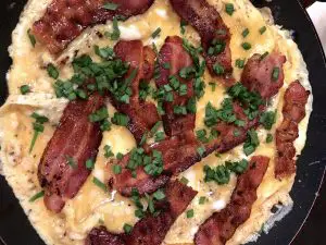 egg and bacon pancake setting in a skillet with chives on top