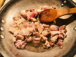 chicken sauteeing in a skillet with wooden spoon