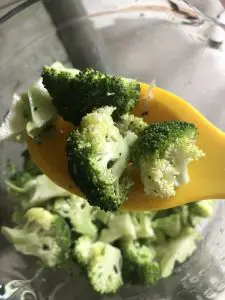 Cut up broccoli florets on top of a yellow spoon