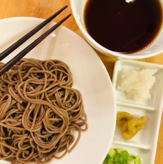 soba noodles in a white bowl with chopsticks, white bowl with soba sauce, and daikon, wasabi, and scallions on a white serving tray