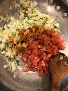 Minced chilies, garlic, and onion, diced tomatoes and spices in a skillet with a wooden spoon