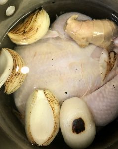 Whole chicken in a stock pot with water, charred onion, and ginger