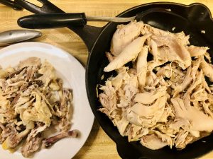 Chicken meat in a cast iron skillet and chicken bones on a white plate