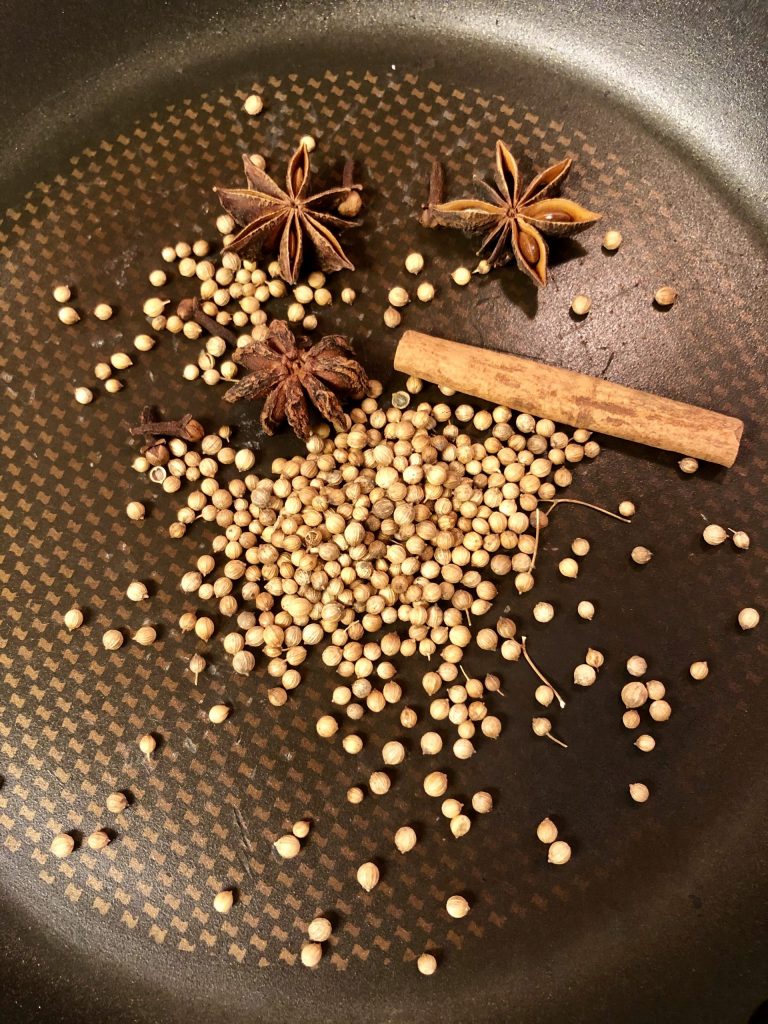 Coriander seed, cinnamon stick, star anise and cloves in a frying pan