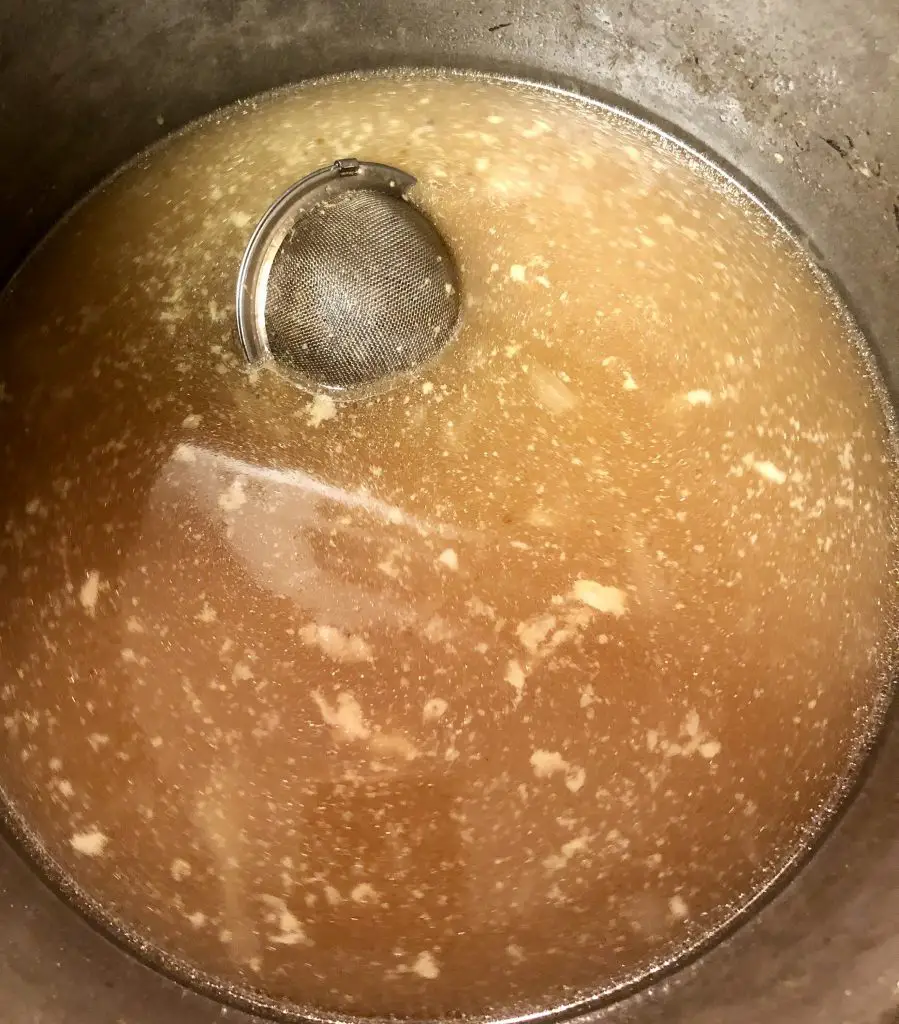 Tea strainer filled with spices in a pho ga broth in a stockpot