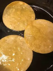 corn tortillas frying in oil in a pan