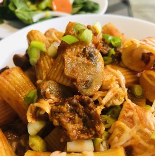 Rigatoni With Sausage in a white bowl with salad in the background