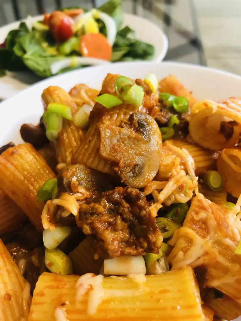 Rigatoni With Sausage in a white bowl with salad in the background