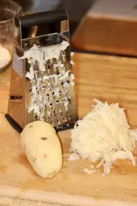 Box grater with a whole peeled potato and grated potato