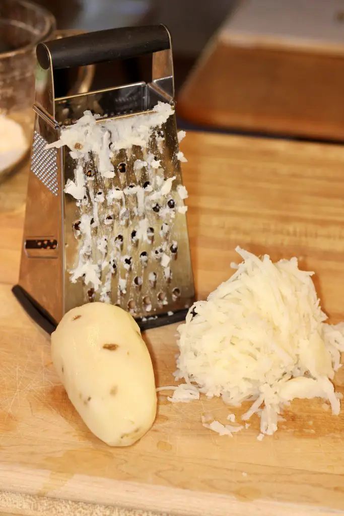 Box grater with a whole peeled potato and grated potato 