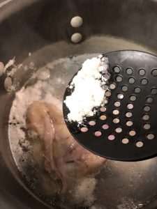 Chicken and water in a stockpot and skimming off scum from the chicken with a utensil