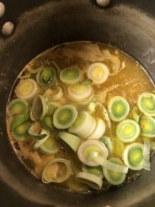 Chicken broth with chopped up leeks in a large stock pot