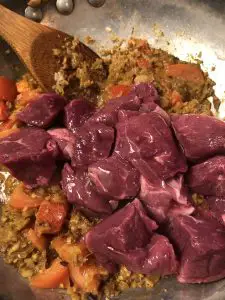 lamb stew meat, onion and tomato spice mixture with a wooden spoon