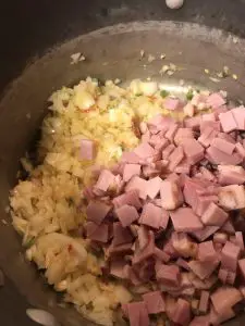 Minced onion, garlic, and Thai chilis, along with diced ham in a saucepan.