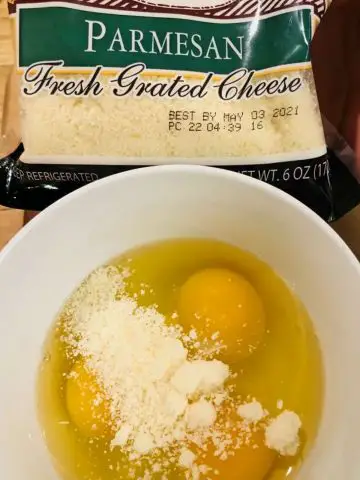 A bag of grated Parmesan cheese and a white bowl containing eggs and Parmesan cheese.