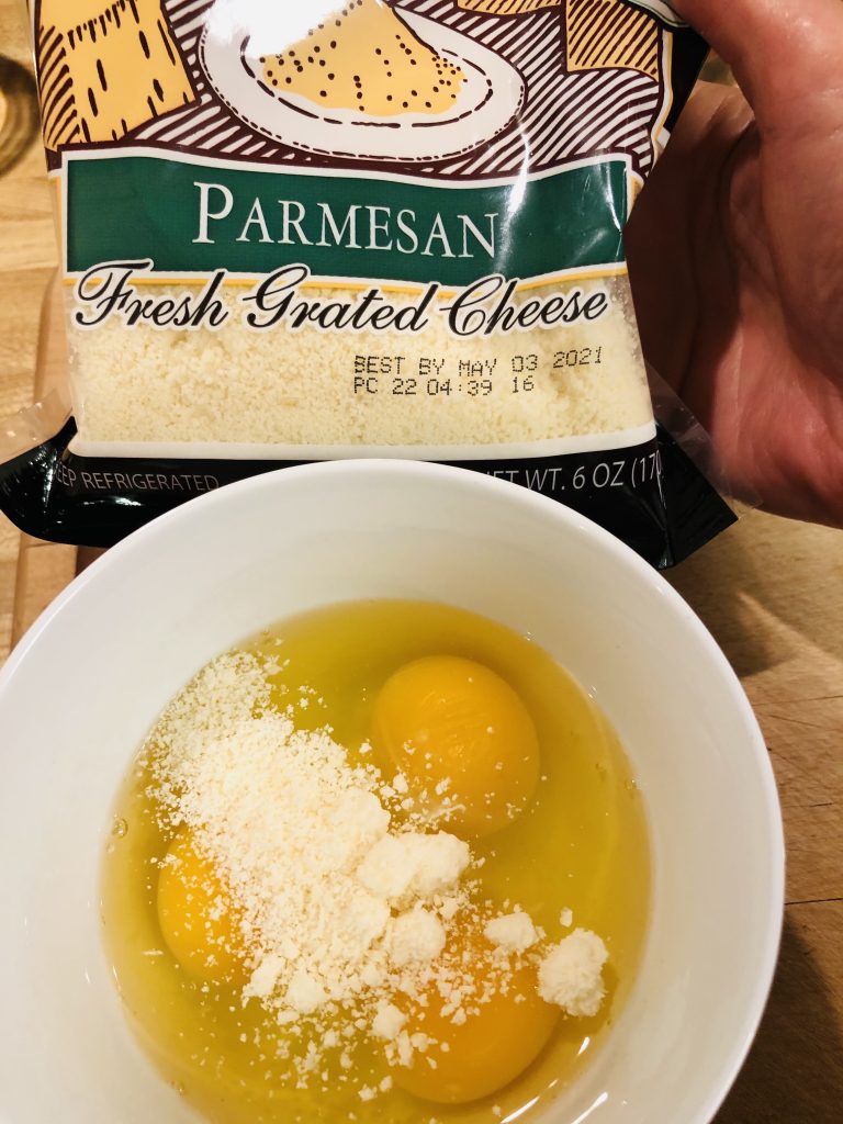 Eggs and parmesan cheese in a white bowl, with a packet of parmesan cheese