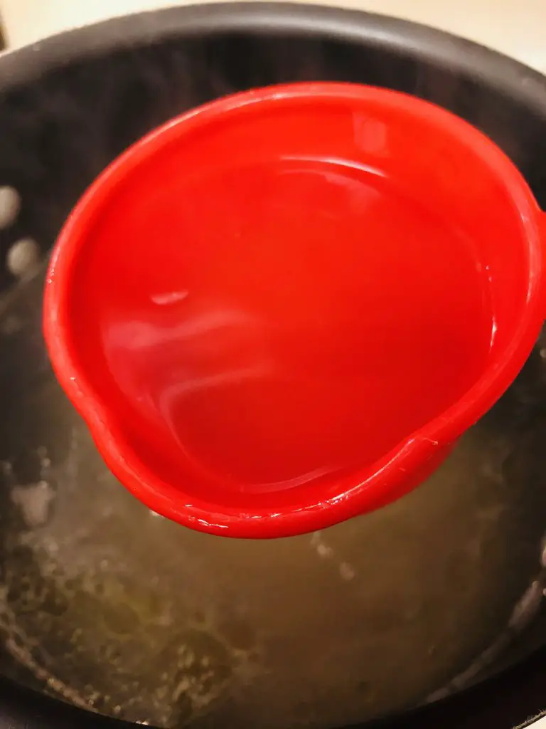 red measuring cup with reserved pasta water