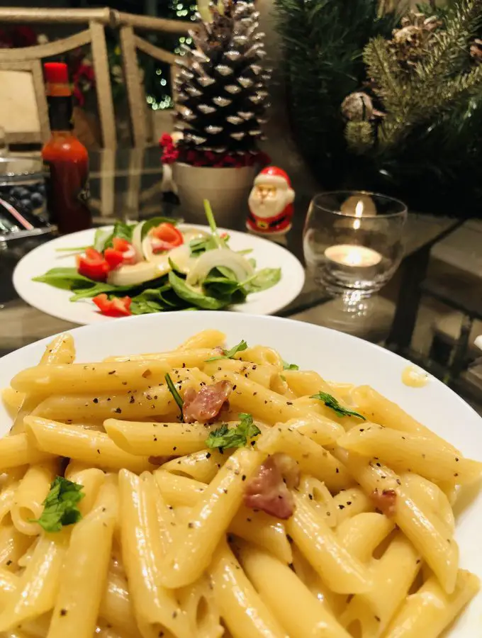 Penne Carbonara with salad, santa claus, tabasco bottle, greenery, and a lit candle in the background