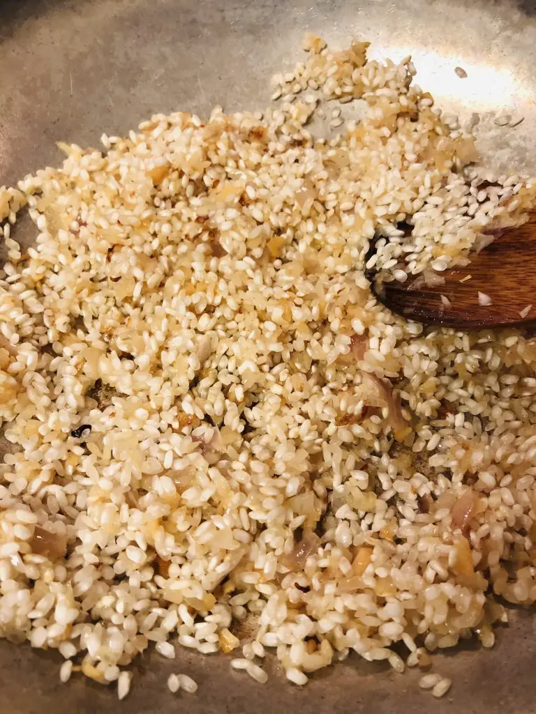 arborio rice, garlic, and shallots in a pan with a wooden spoon