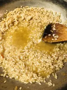 arborio rice absorbing broth in a pan with a wooden spoon