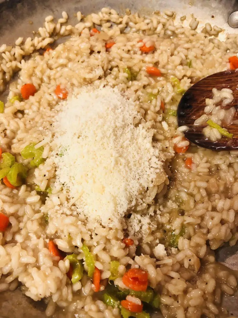 risotto with carrots, celery, and parmesan cheese in a pan with a wooden spoon