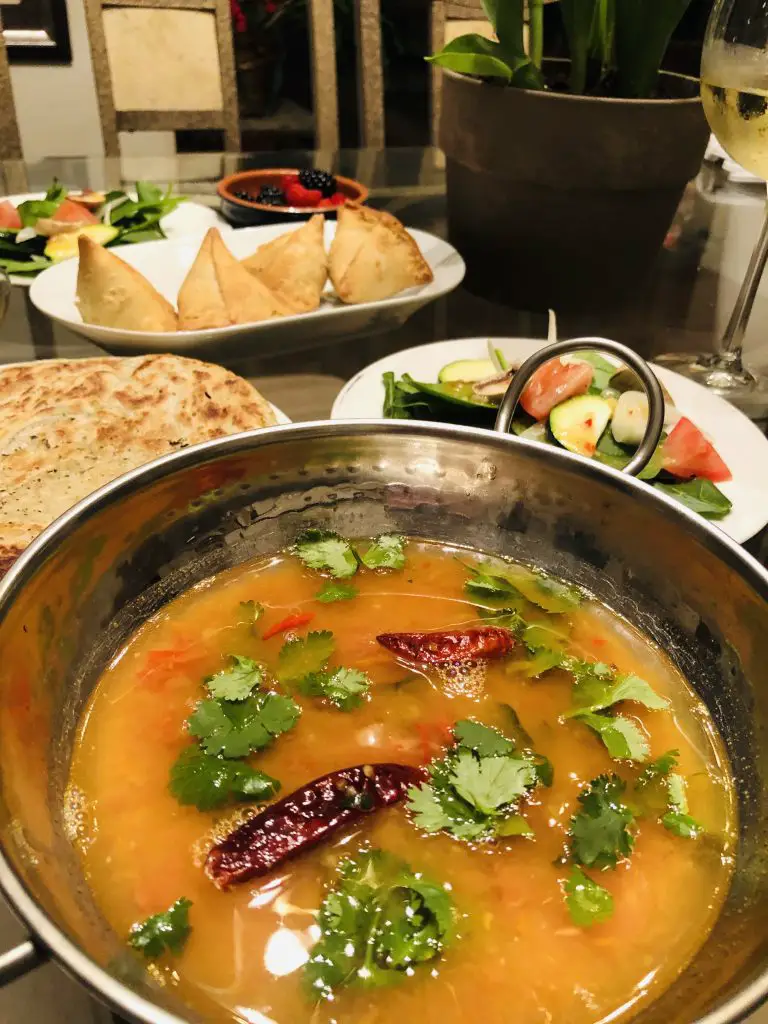 Khatti Daal with salad, paratha, and samosas in the background