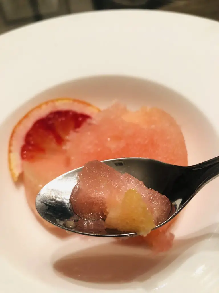 Ciao bella sorbetto and slice of blood orange in a white bowl, and some sorbetto in a spoon