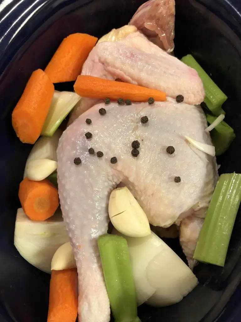 Stewing hen in a crockpot with celery, carrots, onion, garlic and peppercorns