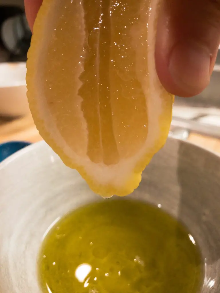 Lemon held above a white bowl containing olive oil