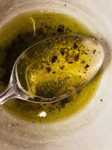 Olive oil based dressing in a white bowl with a spoon