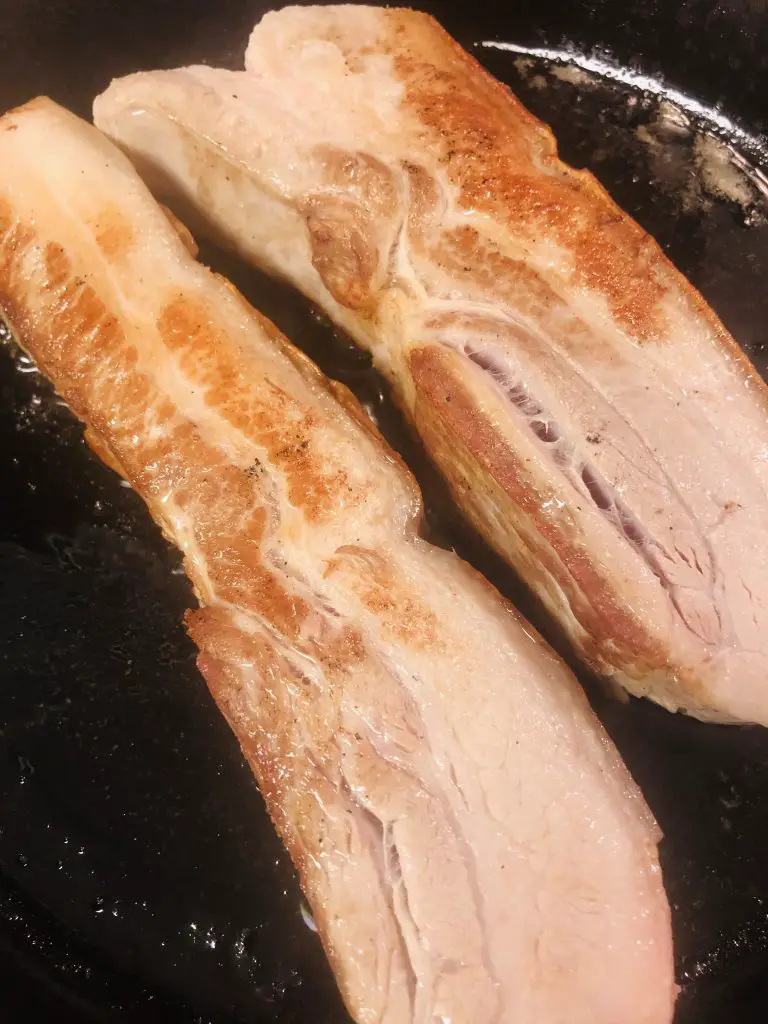 Browned pork belly slabs in a cast iron pan
