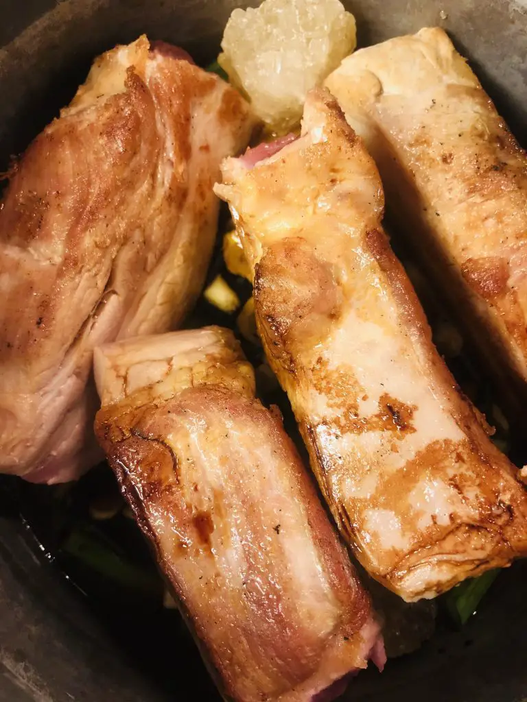 4 pieces of browned pork belly and rock candy on top of ingredients in a saucepan