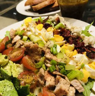 Cobb Salad on a white place with vinaigrette and slices of rye bread in the background