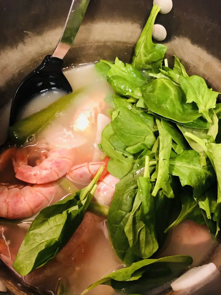 prawn sinigang in a pot with spinach added at the end of cooking time 