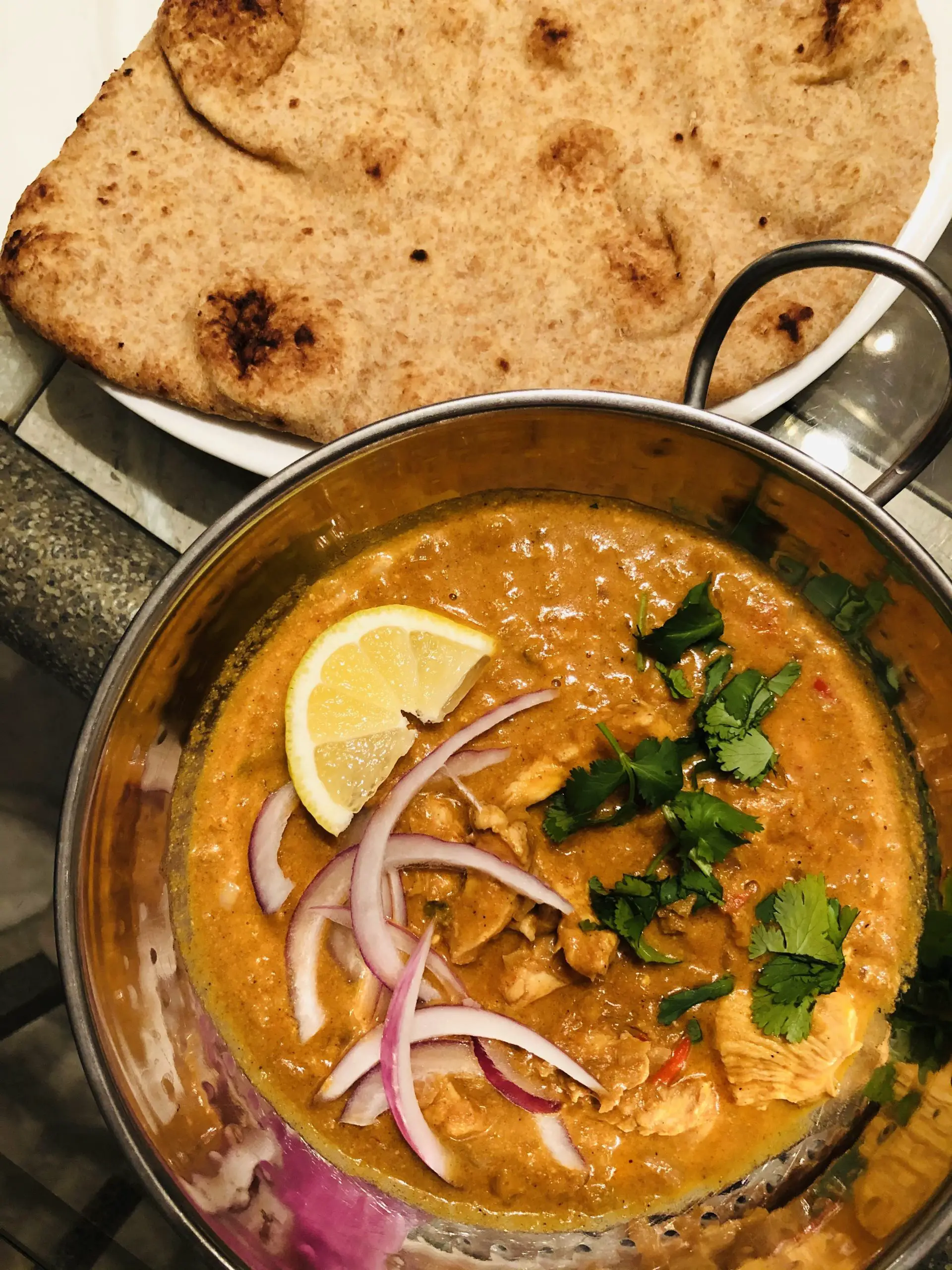Indian Butter chicken in a balti bowl with naan on a white plate