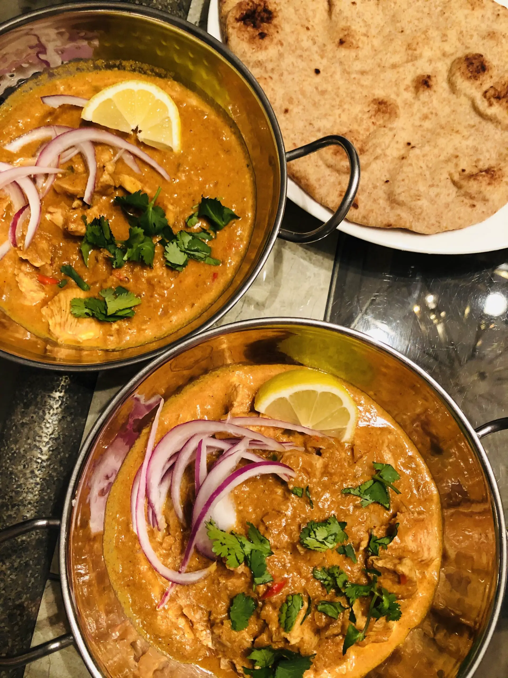 Indian Butter chicken in balti bowls with a naan bread on a white plate