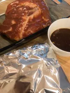 ribs wrapped in foil and ribs on the side along with marinade in a small white bowl