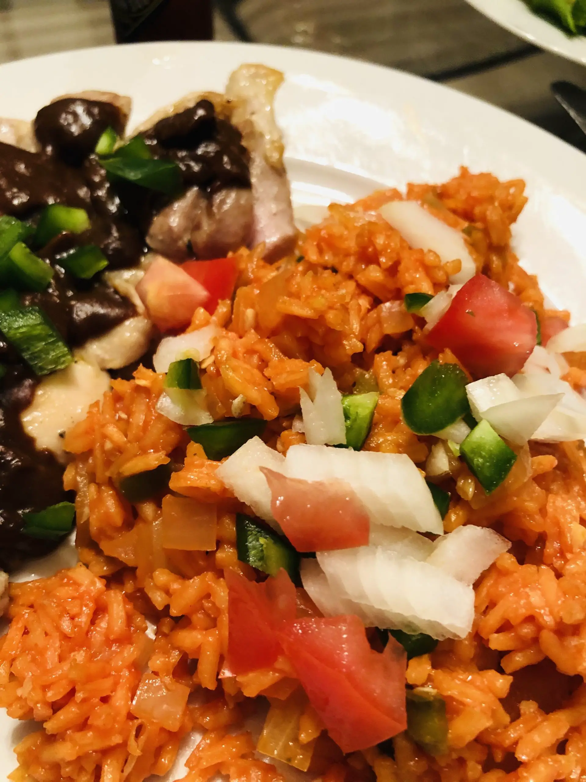 Mexican Rice served with chicken mole on a white plate garnished with onions, tomatoes, and jalapenos