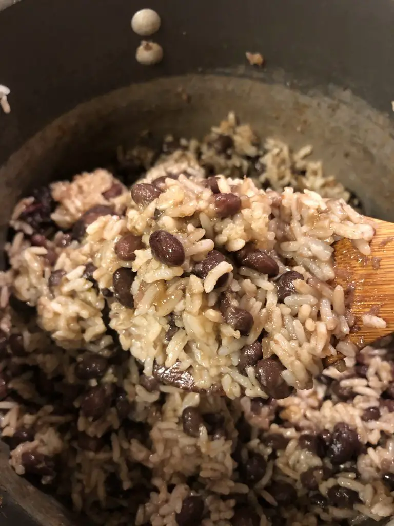 Cuban Black Beans and Rice in a saucepan with a wooden spoon with some of the beans and rice on it in the foreground