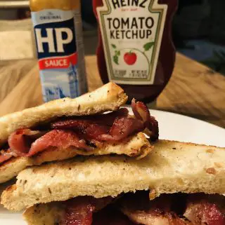 Bacon Sarnie on a white plate with HP Sauce and Heinz Tomato Ketchup in the background