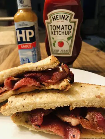 Bacon Sarnie on a white plate with HP Sauce and Heinz Tomato Ketchup in the background