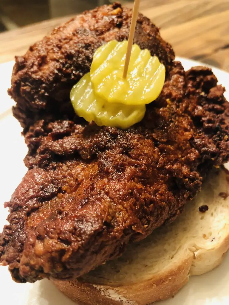 Nashville Hot Chicken on a slice of white bread with pickles on top pierced with a toothpick