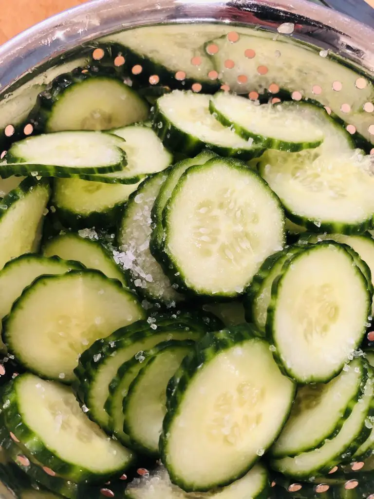 thinly sliced cucumber with salt in a colander