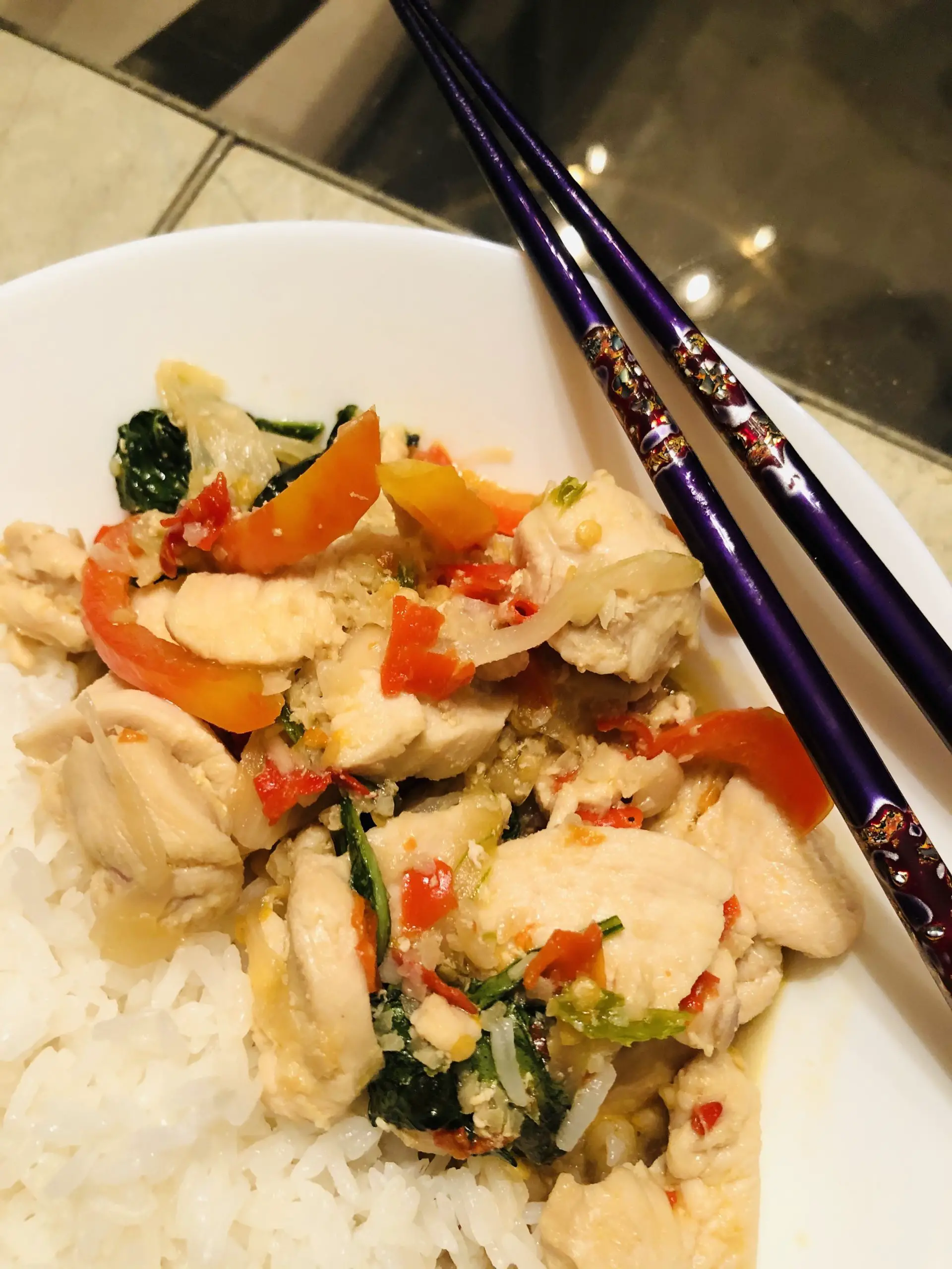 Chicken With Thai Basil served with rice in a white bowl with a pair of purple chopsticks on the side