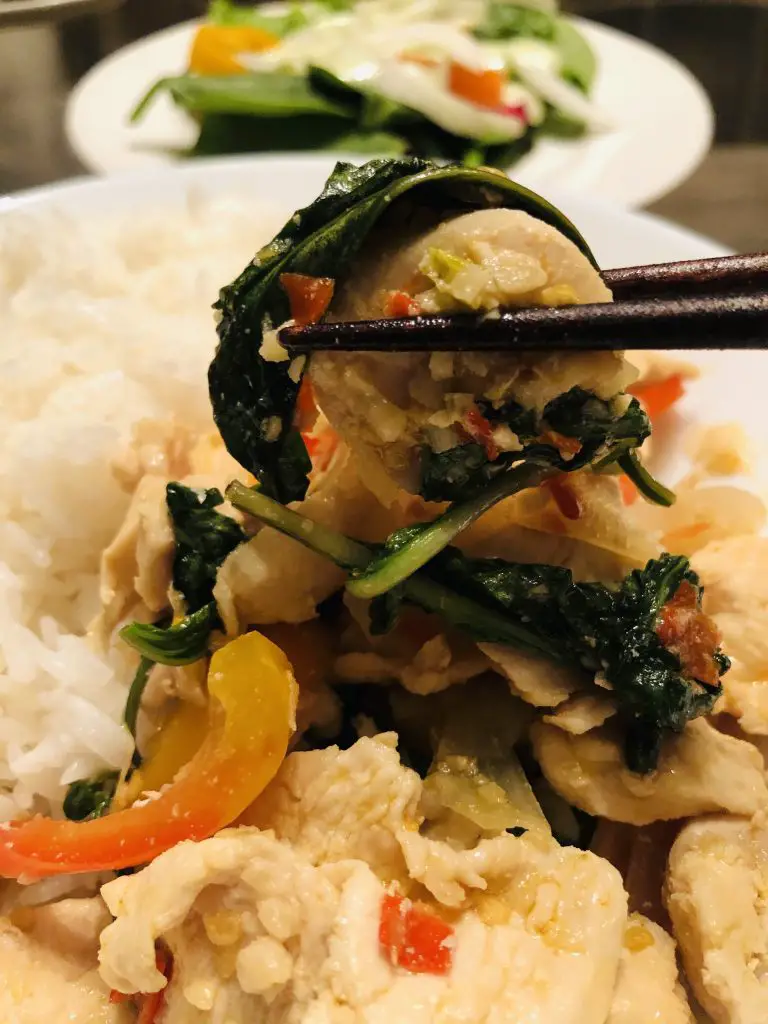 Chicken With Thai Basil served with rice and pair of chopsticks holding up the chicken