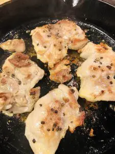 Chicken thighs browning in oil in a cast iron pan