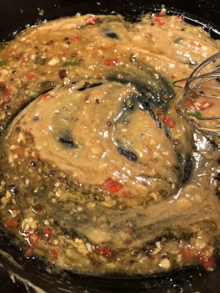 Sauce including garlic, chilies, honey, and dijon mustard in a cast iron skillet with a whisk