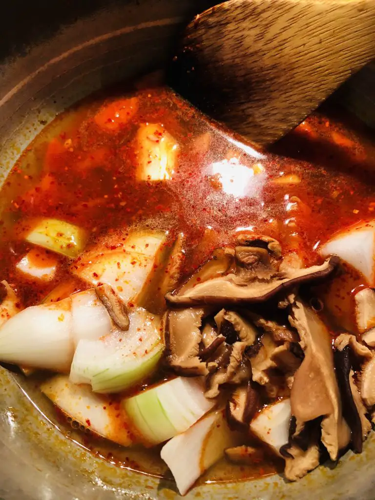 Anchovy broth, gochugaru, gochujang, onions, shiitake mushrooms in a saucepan